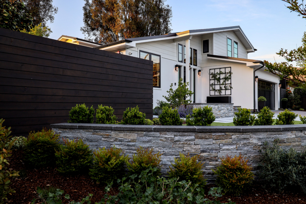 Modern custom home exterior by Montgomery Robbins with sleek black wood fencing, stone retaining wall, and contemporary landscaping