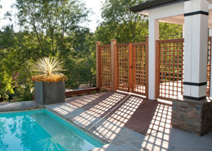 Lattice wood gate casts unique shadows over flush wood deck and bluestone patio where it meets the pool