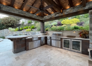 Custom stone and wood pavilion shades outdoor kitchen with grill, sink, storage and drinks fridge