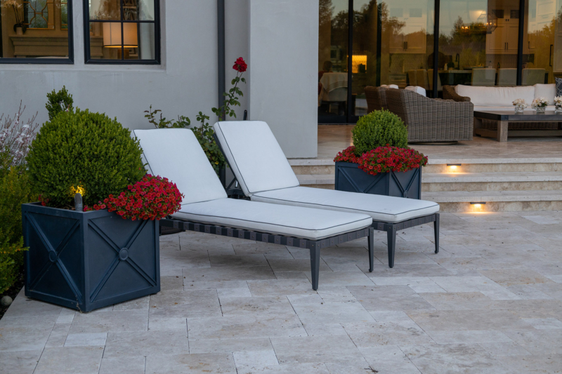 Elegant patio with lounge chairs, planters, and stone flooring by Montgomery Robbins – luxury outdoor living space design