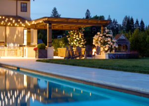 Landscape lighting illuminates an elegant wood pergola with climbing roses