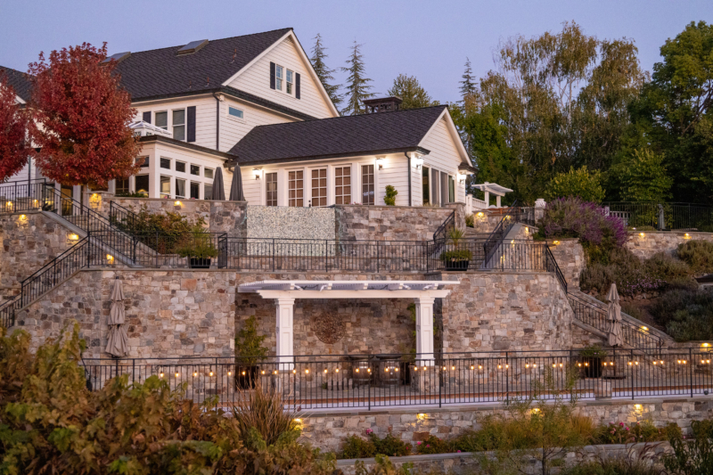 Multi-level stone terrace and hillside landscape design with pergola and ambient lighting by Montgomery Robbins.