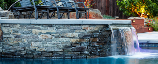 Sheer descent fall cascades into pool from stone-accented upper patio