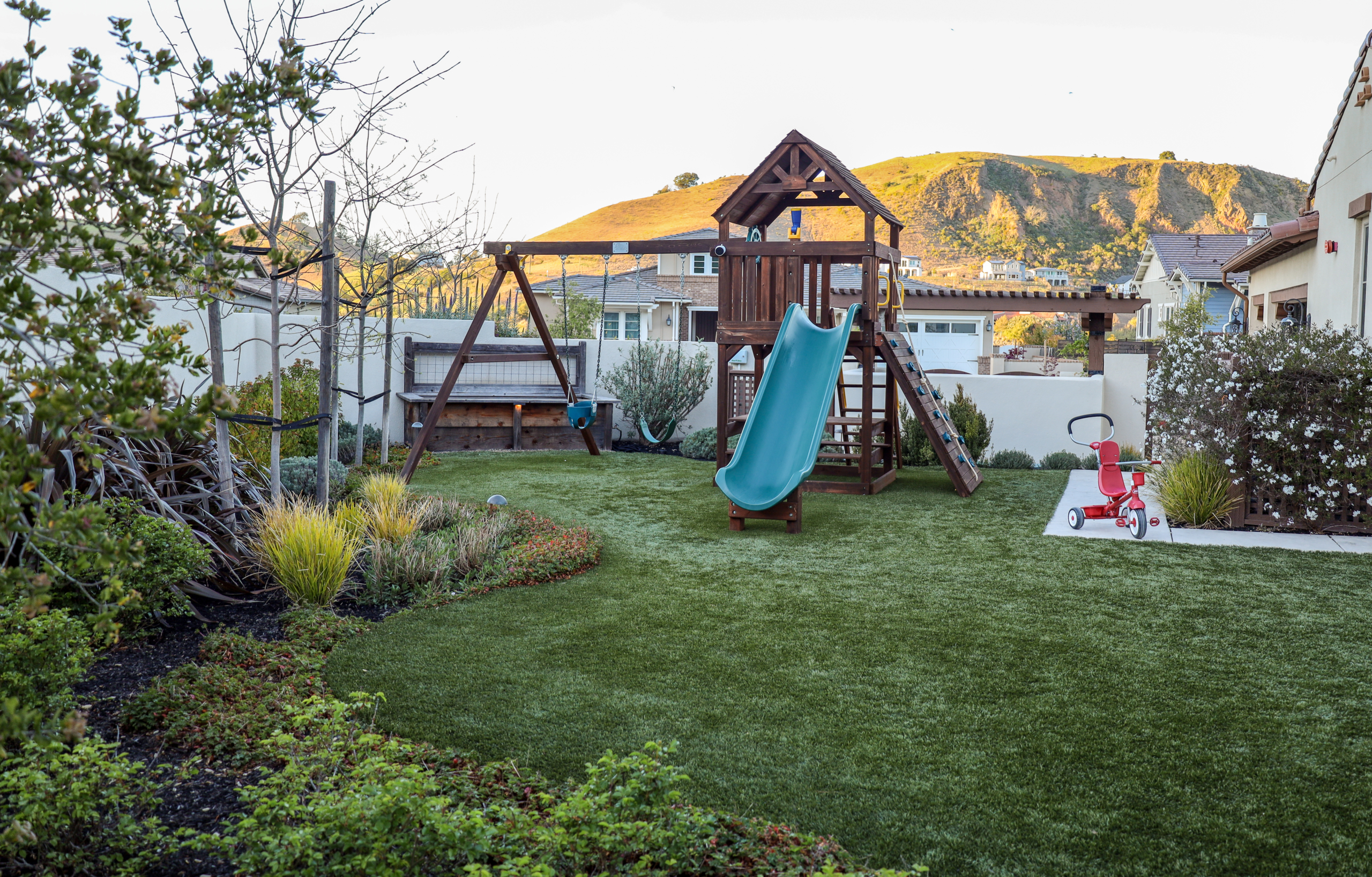 Montgomery Robbins, Inc. landscape architecture design featuring a family-friendly backyard with custom play structure, swing set, artificial turf, and lush planting beds, creating a safe and stylish outdoor living space in Northern California.