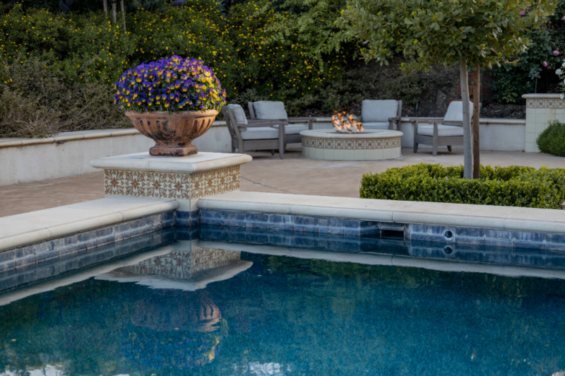 Luxury backyard with tiled pool, fire pit seating, and potted flowers by Montgomery Robbins – custom outdoor living design with Mediterranean flair