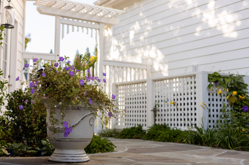 Charming garden pathway with potted flowers and white trellis by Montgomery Robbins – elegant residential landscape design