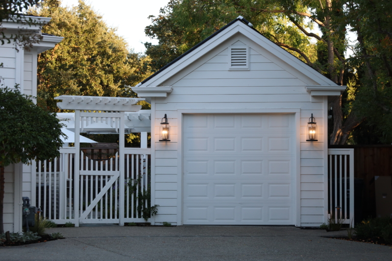 Charming white detached garage and gated entry with modern lantern lighting by Montgomery Robbins