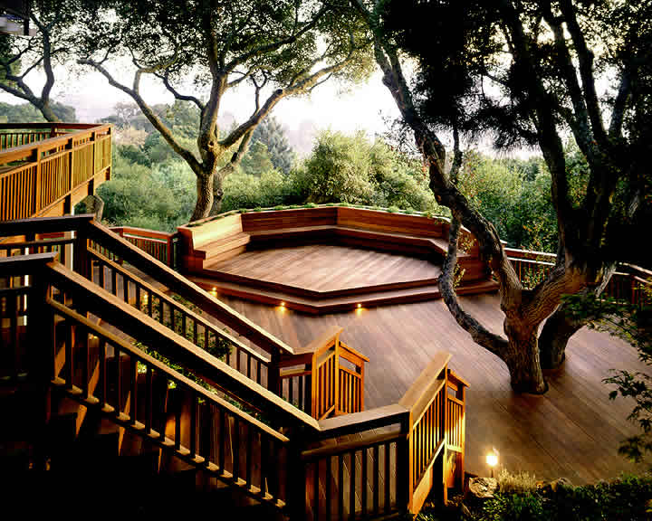 Custom-built wooden deck with built-in seating under mature trees by Montgomery Robbins.