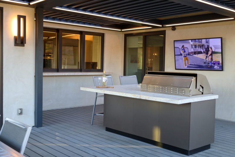 Outdoor kitchen with modern grill island and TV setup by Montgomery Robbins.