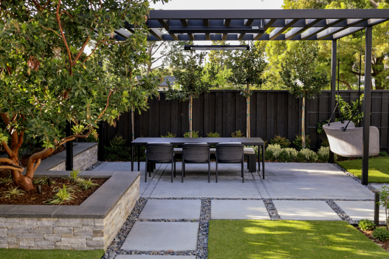 Modern outdoor dining area with pergola and landscaping by Montgomery Robbins featuring concrete pavers and custom seating.