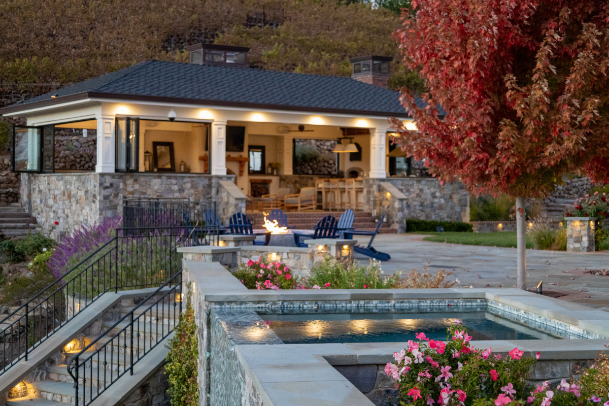 Luxury outdoor living space by Montgomery Robbins featuring a poolside spa, fire pit, and covered patio with custom stonework and fall landscaping.