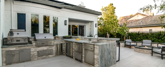 Luxe outdoor kitchen with BBQ, grill, fridge and bar seating on paver patio