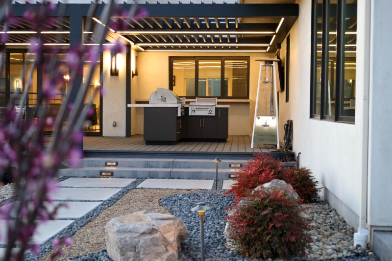 Modern outdoor kitchen and patio design by Montgomery Robbins with built-in grill, pergola, and illuminated landscaping.