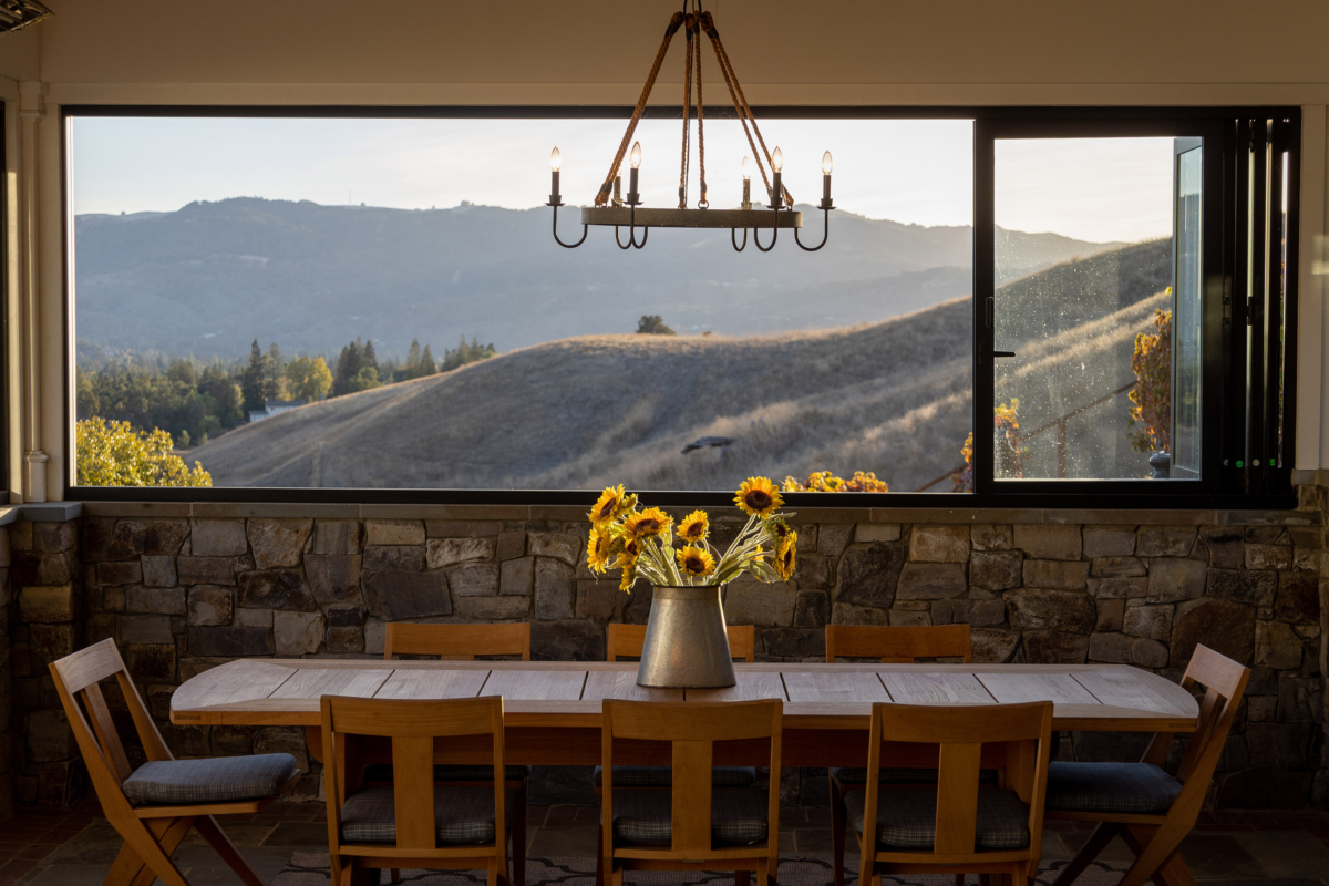 Rustic dining area with mountain view, stone wall, and sunflower centerpiece by Montgomery Robbins – scenic indoor-outdoor living design
