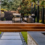 Elegant wood deck with full-length steps meets with contemporary concrete pavers, faux turf and river rock detailing