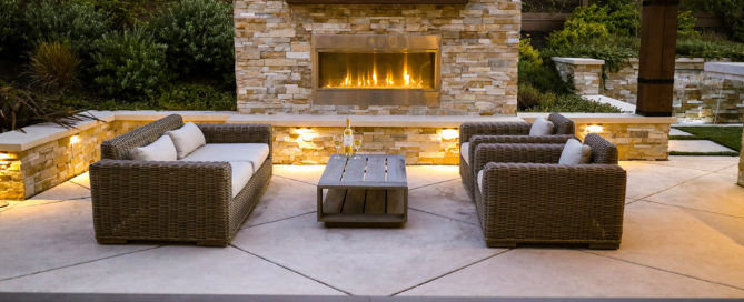 Luxe outdoor fireplace in stone veneer with wood mantle and elegant landscape lighting
