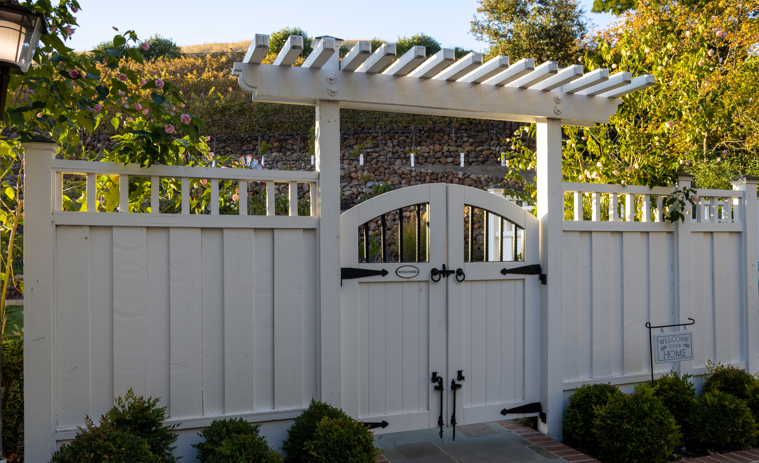 Montgomery Robbins, Inc. landscape architecture design featuring a white wooden garden gate with pergola arbor, classic fencing, climbing vines, and manicured greenery creating a charming entryway to a luxury Northern California backyard.