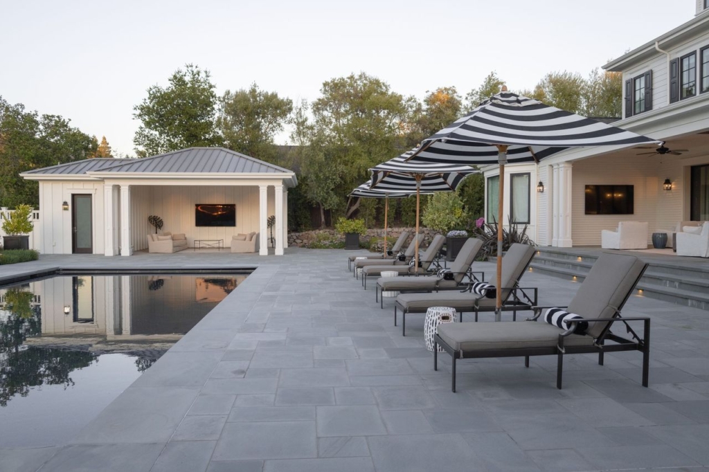 Elegant poolside retreat with striped umbrellas, lounge seating, and modern pool house by Montgomery Robbins Elegant poolside retreat with striped umbrellas, lounge seating, and modern pool house by Montgomery Robbins
