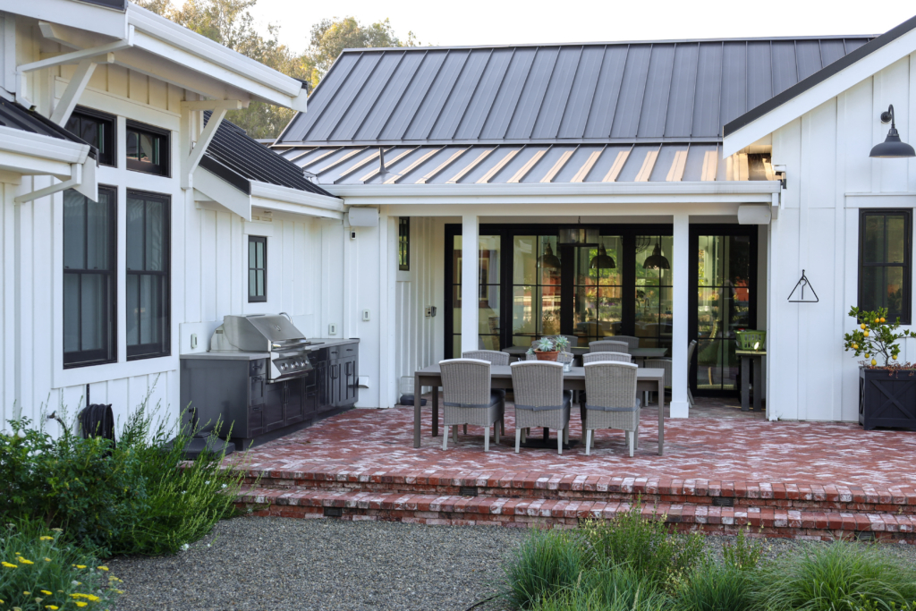 Backyard patio with fire pit, outdoor kitchen, and dining area by Montgomery Robbins